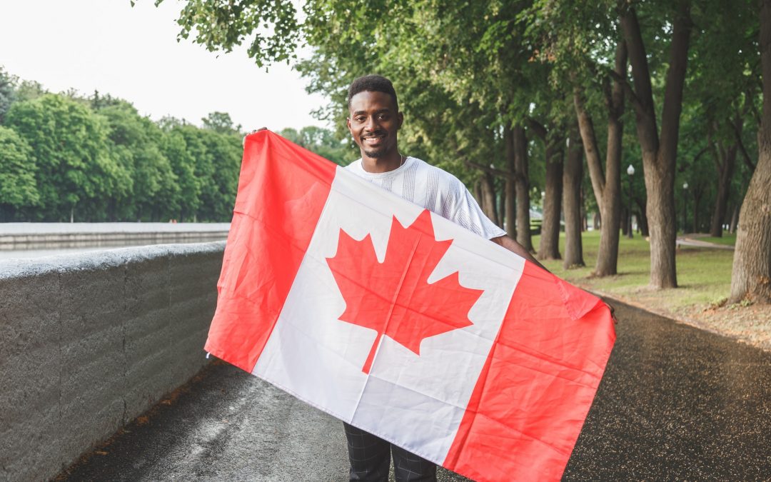 Handsome Afro American man with Canadian flag smiling at camera, standing outdoors.